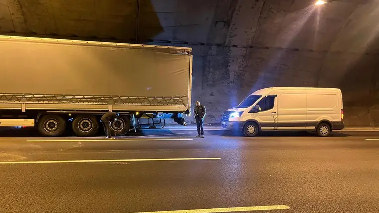 Otoyol kenarında bir aracın lastiği yerinde değiştiriliyor; ekipmanlı servis aracı ve güvenlik konisi görünüyor.