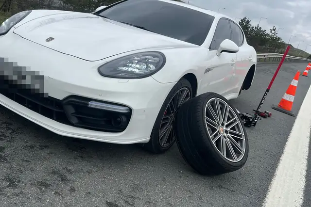 Yol kenarında bir binek aracın sökülmüş tekerleği yere yatırılmış; kriko aracın altında, arkada güvenlik konileri sıralı.