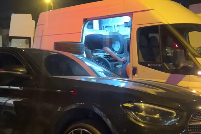 Gece, yan kapısı açık servis aracının içinde lastik makinesinin başında çalışılıyor; kapının önünde bir lastik, önde siyah bir otomobil.